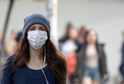 Woman wearing a face mask, with ear phones and a beanie