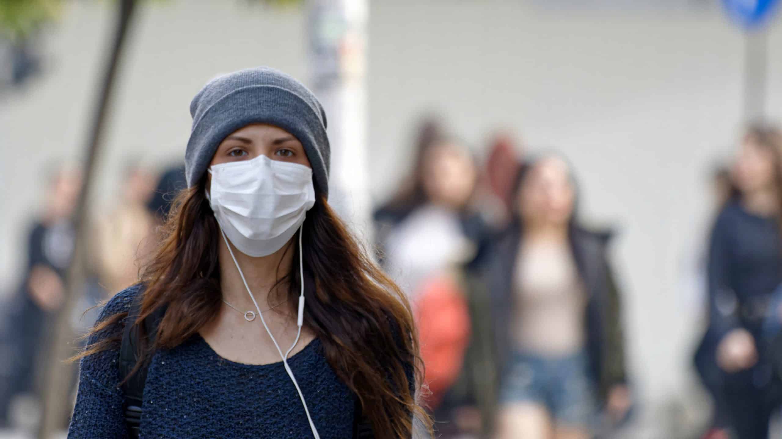 Woman wearing a face mask, with ear phones and a beanie