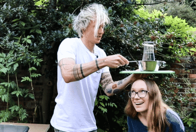 Tom holding a glass of water and a colander over Fiona's head!