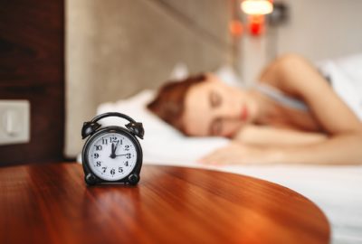 Woman sleeping, with an alarm clock by her bed.