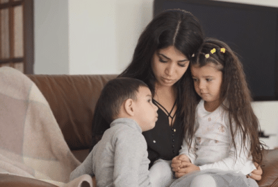 A mother talks to two children on the sofa. Featured image for the video 'What do we tell the children?'