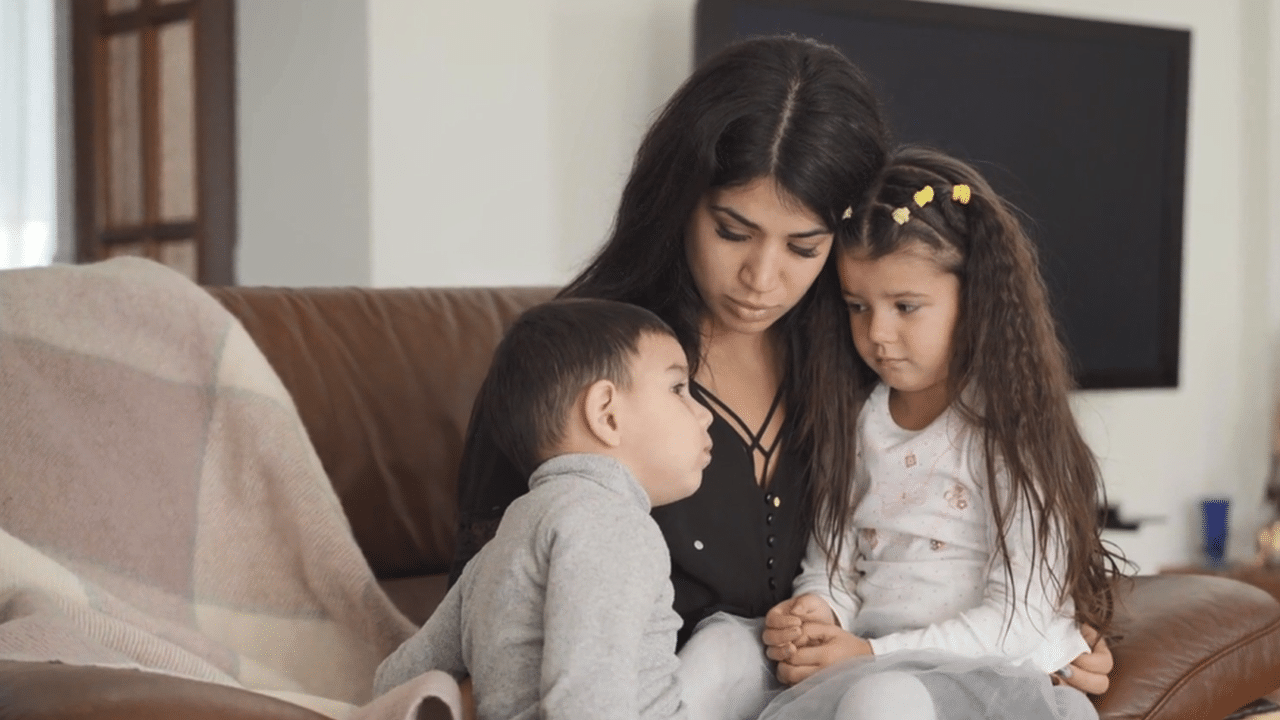 A mother talks to two children on the sofa. Featured image for the video 'What do we tell the children?'