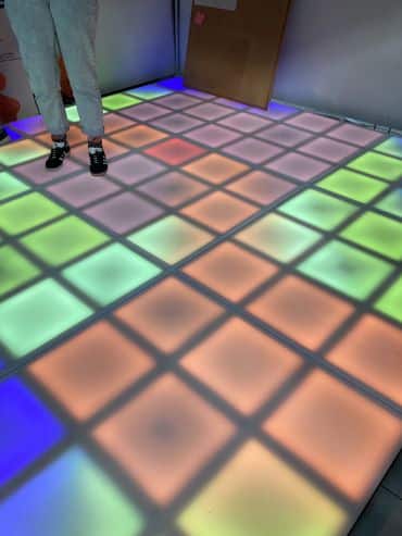 A person stands on a floor made up of illuminated tiles of different colours.