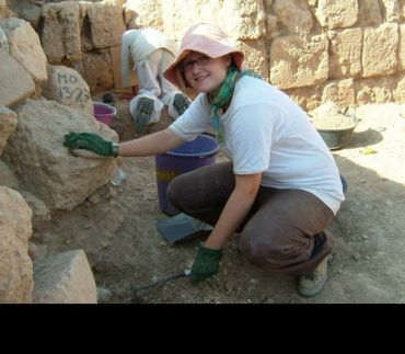 A woman crouches down next to an ancient brick wall in a dry, arid environment.