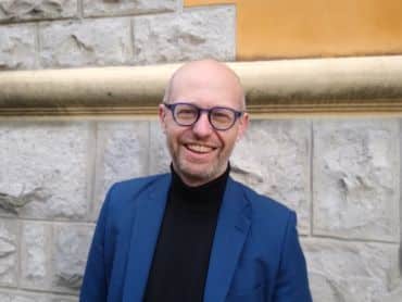 A portrait photograph of Professor Richard Walker, standing by a brick wall.