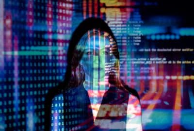 Computer code in different colours is projected on to the face of a woman. Featured image for podcast episode 'Why are deepfakes happening?'