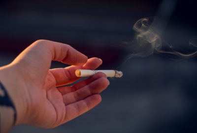 A hand is holding a smoking cigarette.