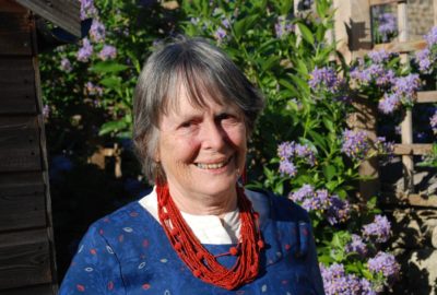 Older woman wearing a dark blue jumper and red necklace is smiling