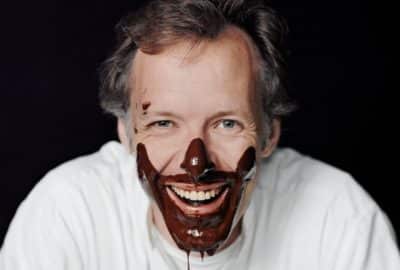 A man is smiling at the camera with chocolate dripping off his face.