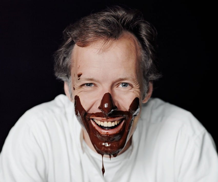 A man is smiling at the camera with chocolate dripping off his face.
