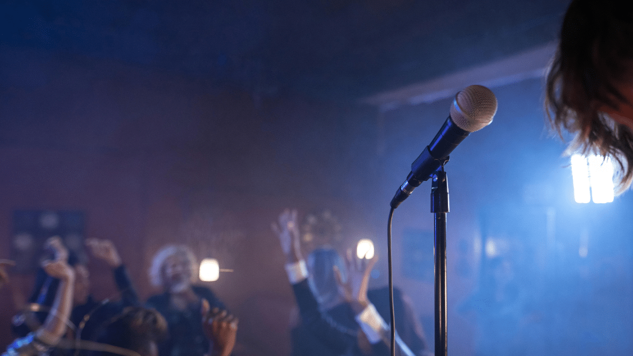 AI generated image of a stand up comedy club. The image shows a microphone, with a blurred audience in the background.