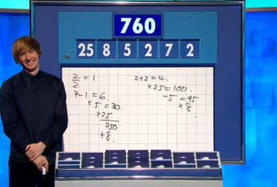 Dr Tom Crawford stands, smiling, in front of the Countdown numbers board.