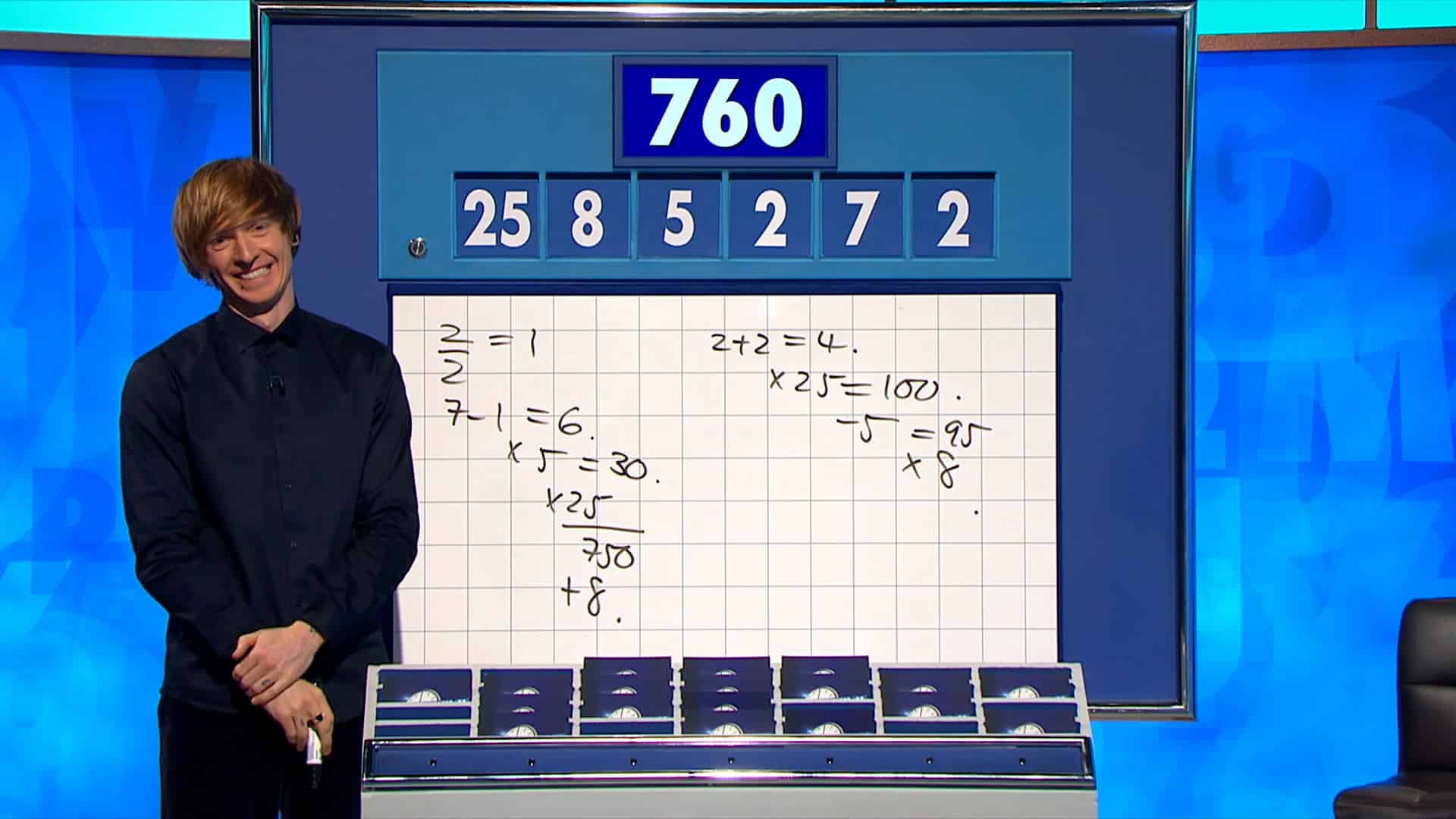 Dr Tom Crawford stands, smiling, in front of the Countdown numbers board.