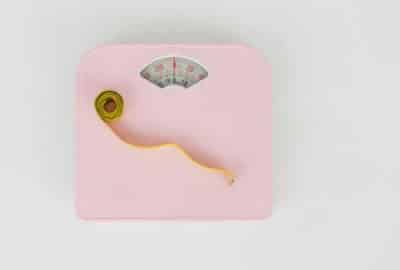 A curled up tape measure sits of a set of pink weighing scales
