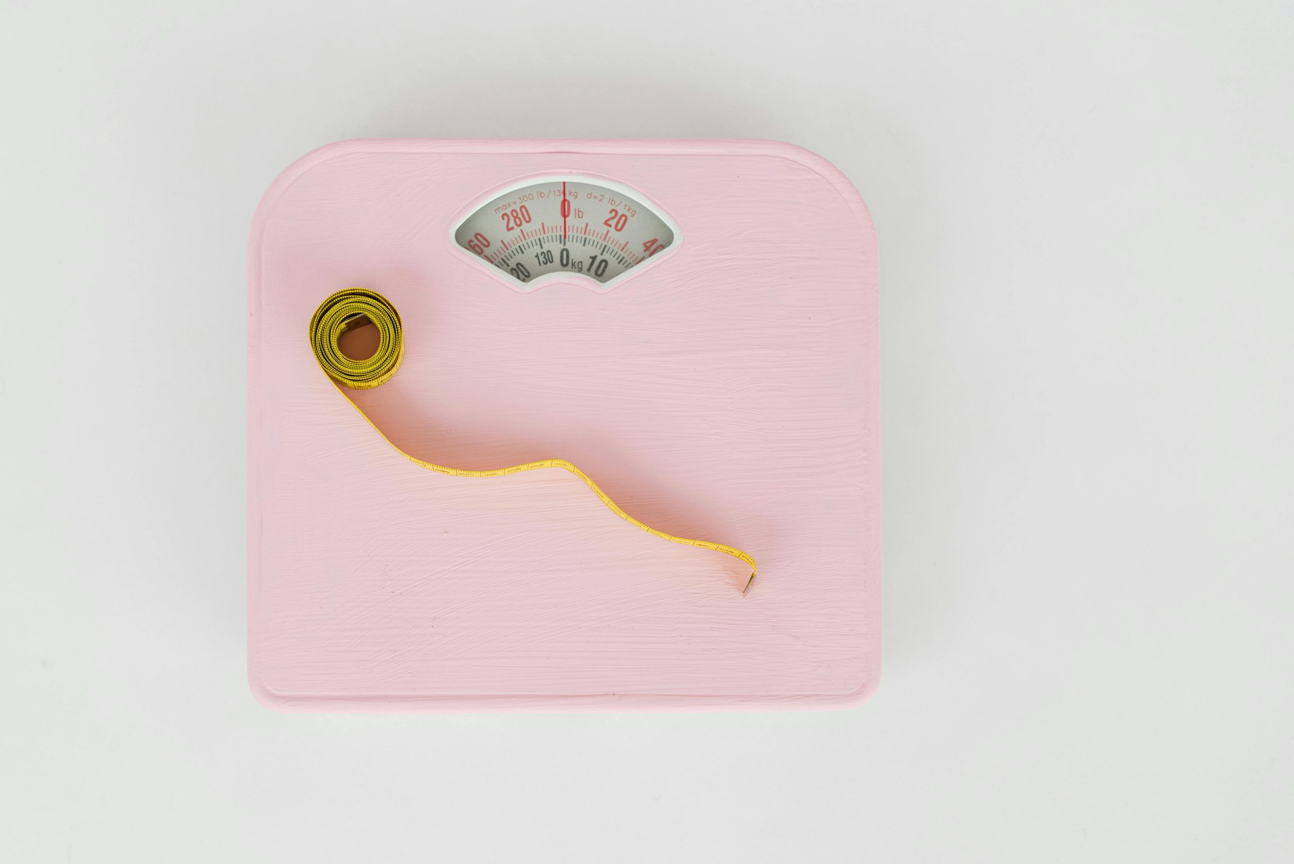 A curled up tape measure sits of a set of pink weighing scales