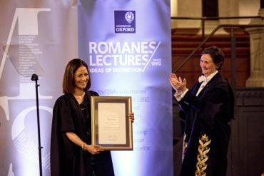 Image of the Vice-Chancellor Professor Irene Tracey and Mishal Husain on stage, with the Vice-Chancellor applauding Mishal Husain who's holding her framed certificate for delivering the Romanes Lecture 2025