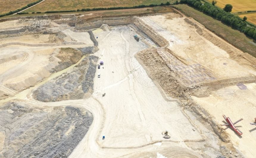 Aerial shot of a rectangular excavation in a quarry with lines of exposed dinosaur footprints running along the length. Members of the excavation team are in shot.