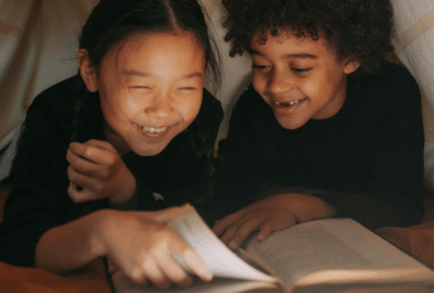 Two girls laugh as they turn the pages of a book.