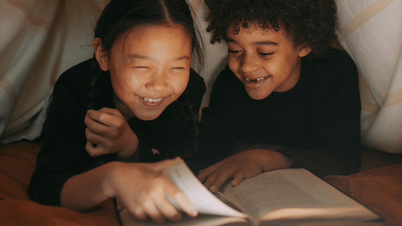 Two girls laugh as they turn the pages of a book.