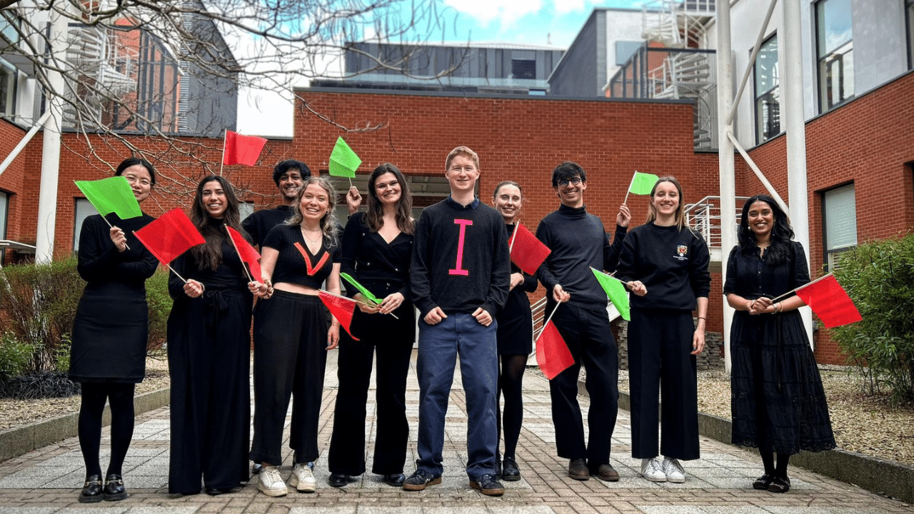 A group of young people dressed in black and holding red and green flags. (The team use these flags to demonstrate the body's immune system response to precancer and cancer vaccines in the video).